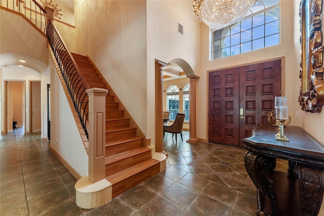 entryway with a towering ceiling, an inviting chandelier, and ornate columns