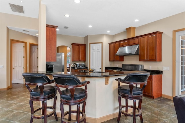 kitchen featuring kitchen peninsula, a breakfast bar area, appliances with stainless steel finishes, and dark stone counters