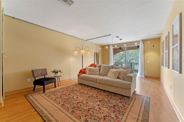 living room with a textured ceiling, light hardwood / wood-style flooring, and ceiling fan