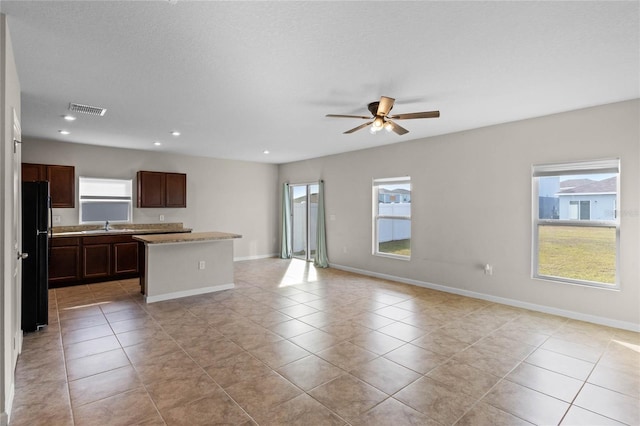 kitchen with black refrigerator, a center island, ceiling fan, and light tile patterned flooring