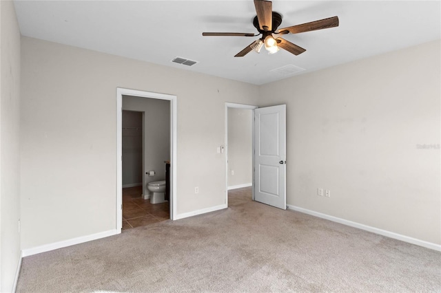 unfurnished bedroom with a walk in closet, ensuite bathroom, light colored carpet, ceiling fan, and a closet