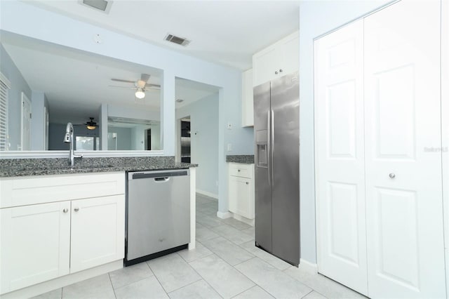 kitchen with dark stone counters, white cabinets, sink, light tile patterned floors, and stainless steel appliances