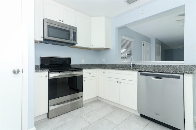 kitchen with light tile patterned floors, stainless steel appliances, white cabinetry, and dark stone countertops