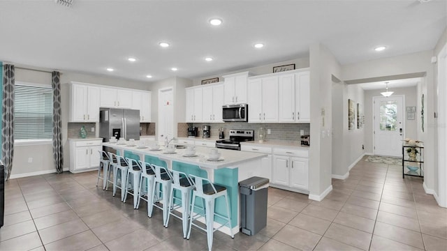 kitchen featuring a kitchen breakfast bar, white cabinetry, a center island with sink, and appliances with stainless steel finishes