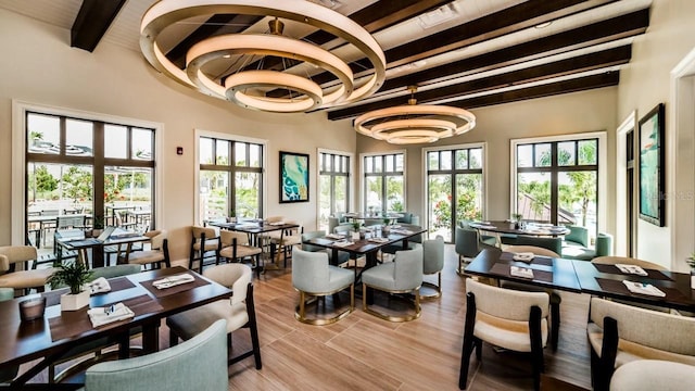 dining space featuring beamed ceiling, light wood-type flooring, and an inviting chandelier