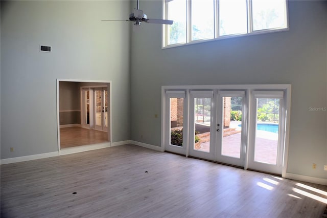 unfurnished living room featuring ceiling fan, a high ceiling, a wealth of natural light, and light hardwood / wood-style flooring