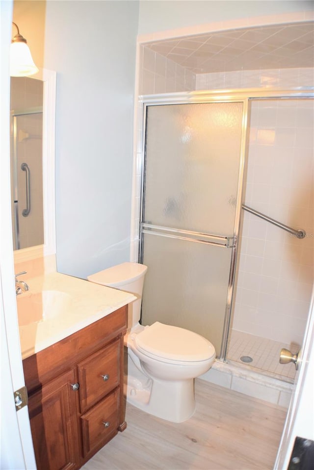 bathroom with hardwood / wood-style floors, vanity, a shower with door, and toilet