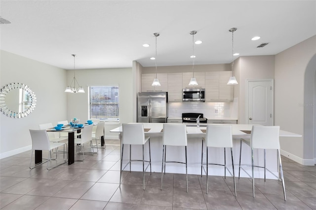 kitchen with backsplash, stainless steel appliances, a kitchen island with sink, decorative light fixtures, and a chandelier