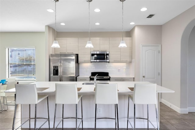 kitchen with hanging light fixtures, appliances with stainless steel finishes, a breakfast bar, and a kitchen island with sink