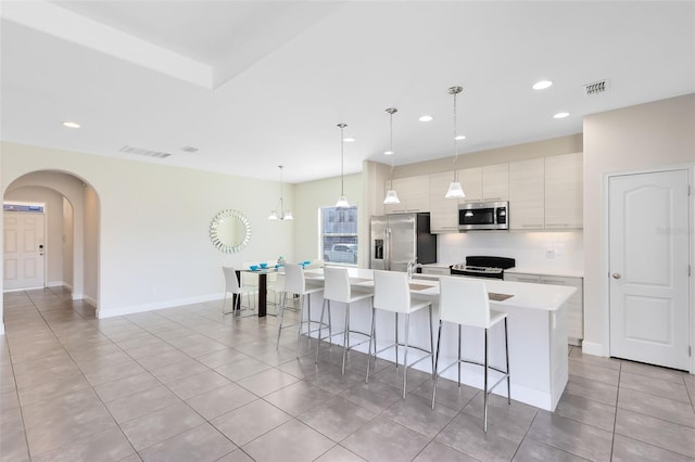 kitchen featuring a kitchen island with sink, light tile patterned floors, appliances with stainless steel finishes, decorative light fixtures, and a breakfast bar area