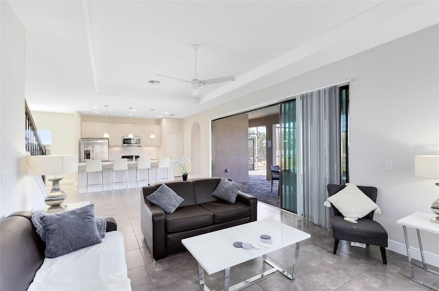 living room with light tile patterned floors, a tray ceiling, and ceiling fan