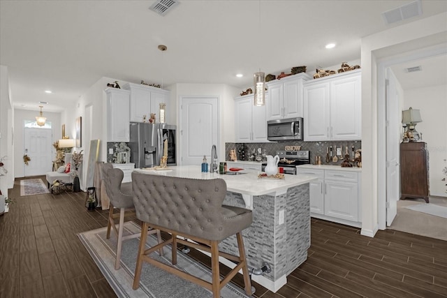 kitchen with dark hardwood / wood-style floors, white cabinetry, an island with sink, and appliances with stainless steel finishes