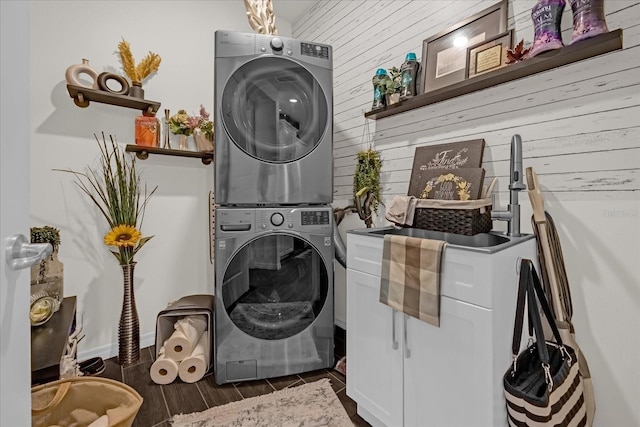 laundry room with cabinets, sink, dark hardwood / wood-style floors, stacked washer / drying machine, and wood walls