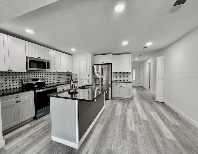 kitchen featuring light wood-type flooring, stainless steel appliances, white cabinetry, and an island with sink