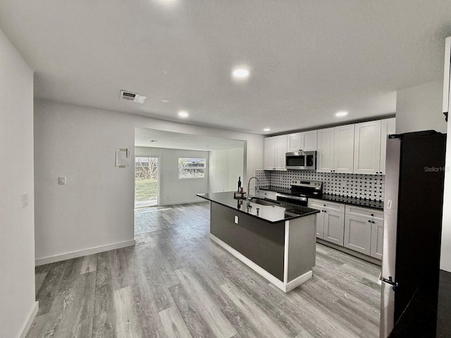 kitchen with backsplash, a kitchen island with sink, light wood-type flooring, white cabinetry, and stainless steel appliances