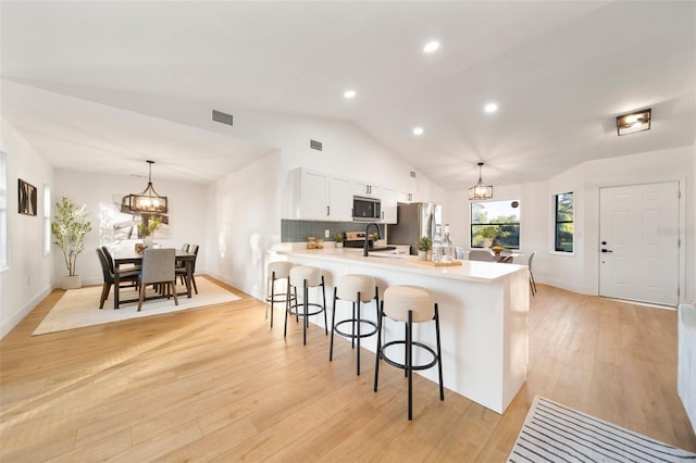 896 Talmadge Ave SE, Palm Bay, FL 32909 - kitchen featuring a kitchen breakfast bar, vaulted ceiling, light wood-type flooring, decorative light fixtures, and white cabinetry