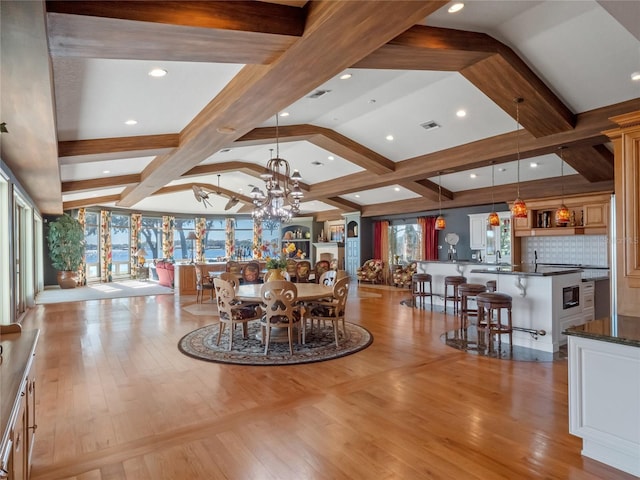 dining space with vaulted ceiling with beams, light hardwood / wood-style flooring, and a chandelier