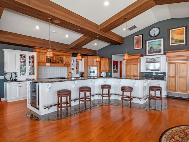 kitchen featuring a breakfast bar, wine cooler, vaulted ceiling with beams, tasteful backsplash, and decorative light fixtures