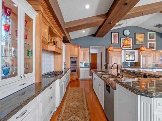 kitchen featuring a large island with sink, lofted ceiling with beams, appliances with stainless steel finishes, decorative light fixtures, and light hardwood / wood-style floors