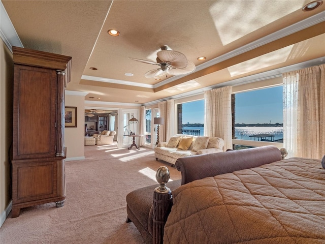 bedroom with ceiling fan, a tray ceiling, light carpet, a water view, and ornamental molding