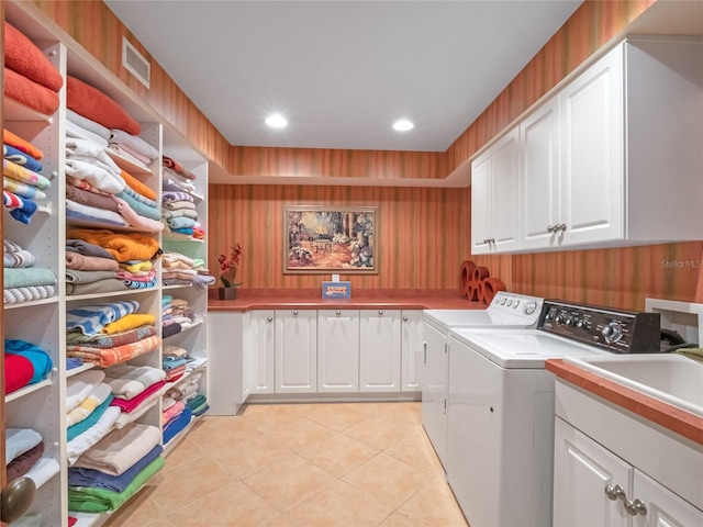 laundry area featuring washing machine and clothes dryer, sink, light tile patterned floors, and cabinets