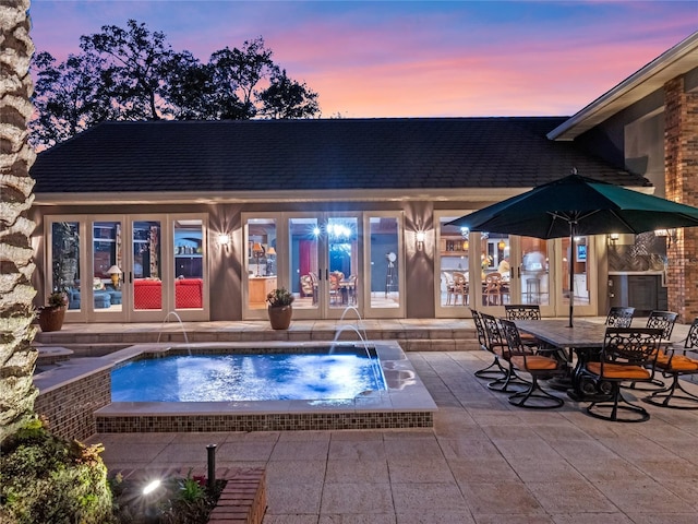 pool at dusk with pool water feature, french doors, and a hot tub