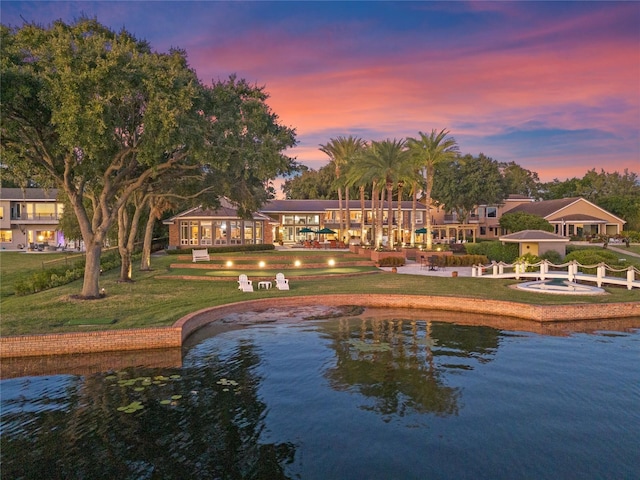 back house at dusk featuring a lawn and a water view