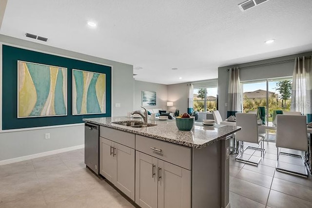 kitchen with light stone counters, stainless steel dishwasher, gray cabinetry, sink, and a center island with sink