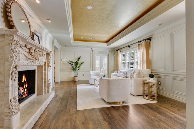 living room featuring hardwood / wood-style flooring, ornamental molding, a raised ceiling, and a premium fireplace