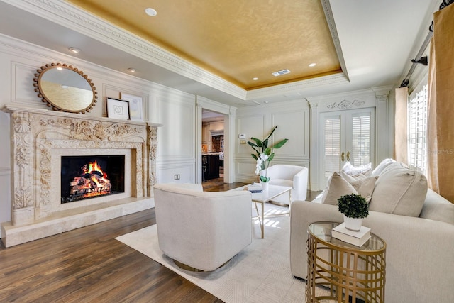 living room with crown molding, a premium fireplace, a tray ceiling, and hardwood / wood-style floors