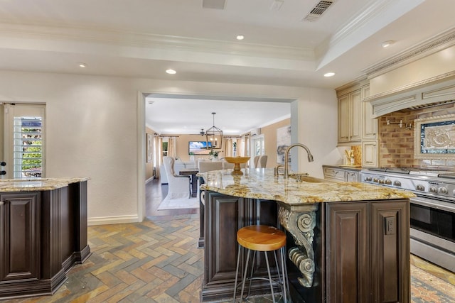 kitchen featuring double oven range, light stone countertops, sink, and an island with sink