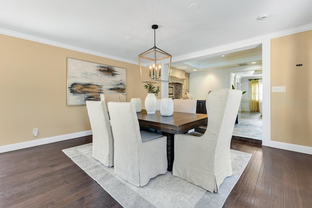 dining space with dark wood-type flooring, ornamental molding, a raised ceiling, and a notable chandelier