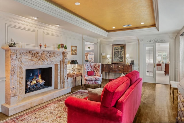 living room featuring crown molding, a fireplace, wood-type flooring, and a tray ceiling