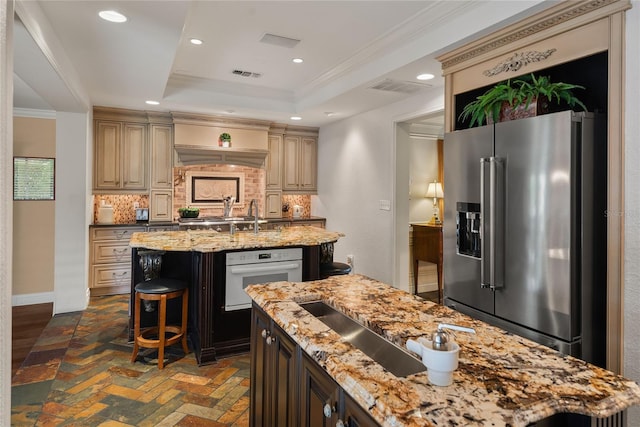 kitchen with white oven, decorative backsplash, light stone counters, a center island with sink, and high end fridge