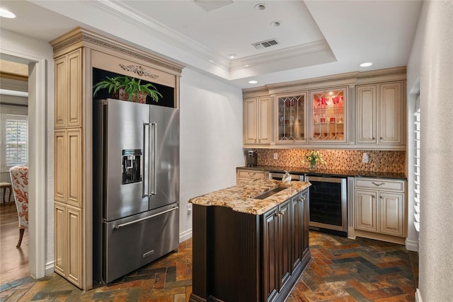 kitchen with a raised ceiling, tasteful backsplash, high quality fridge, ornamental molding, and light stone counters