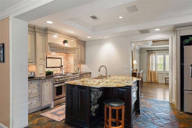 kitchen with light stone countertops, stainless steel appliances, ornamental molding, and an island with sink