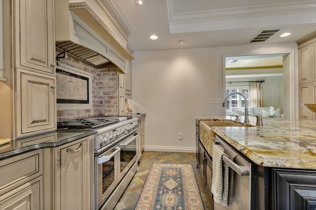 kitchen with custom exhaust hood, sink, light stone countertops, appliances with stainless steel finishes, and cream cabinets