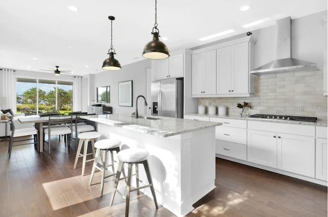 kitchen with wall chimney exhaust hood, stainless steel appliances, sink, white cabinets, and an island with sink