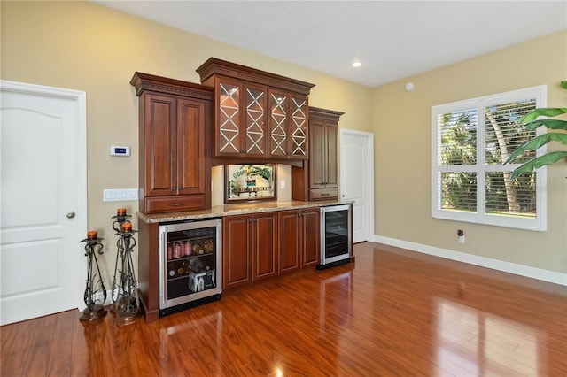 bar with light stone counters, beverage cooler, and dark wood-type flooring