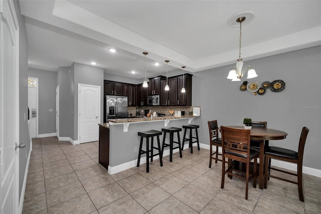 kitchen with kitchen peninsula, hanging light fixtures, appliances with stainless steel finishes, tasteful backsplash, and dark brown cabinetry