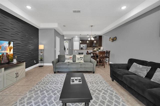 living room featuring a raised ceiling, light tile patterned flooring, and a chandelier