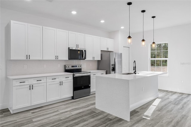 kitchen with white cabinets, appliances with stainless steel finishes, decorative light fixtures, and an island with sink