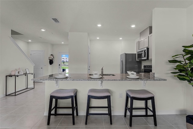 kitchen with kitchen peninsula, a kitchen breakfast bar, stainless steel appliances, stone countertops, and white cabinetry