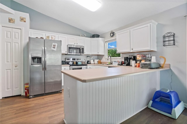 kitchen featuring kitchen peninsula, light wood-type flooring, stainless steel appliances, white cabinetry, and lofted ceiling