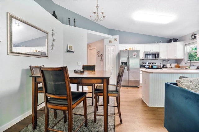 dining area featuring a chandelier, light wood-type flooring, sink, and vaulted ceiling