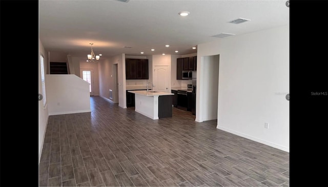 kitchen with dark brown cabinetry, sink, an inviting chandelier, dark hardwood / wood-style flooring, and a kitchen island with sink