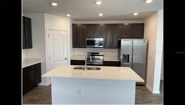 kitchen featuring dark wood-type flooring, sink, light stone countertops, an island with sink, and stainless steel appliances