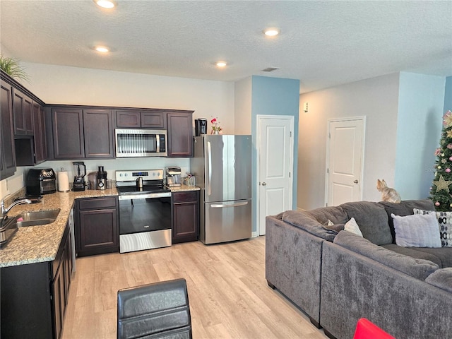 604 Madison Dr, Davenport, FL 33837 - kitchen with stainless steel appliances, open floor plan, dark brown cabinets, light wood-type flooring, and a textured ceiling