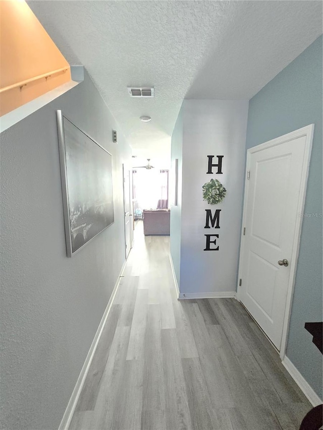 hallway with a textured ceiling and light wood-type flooring