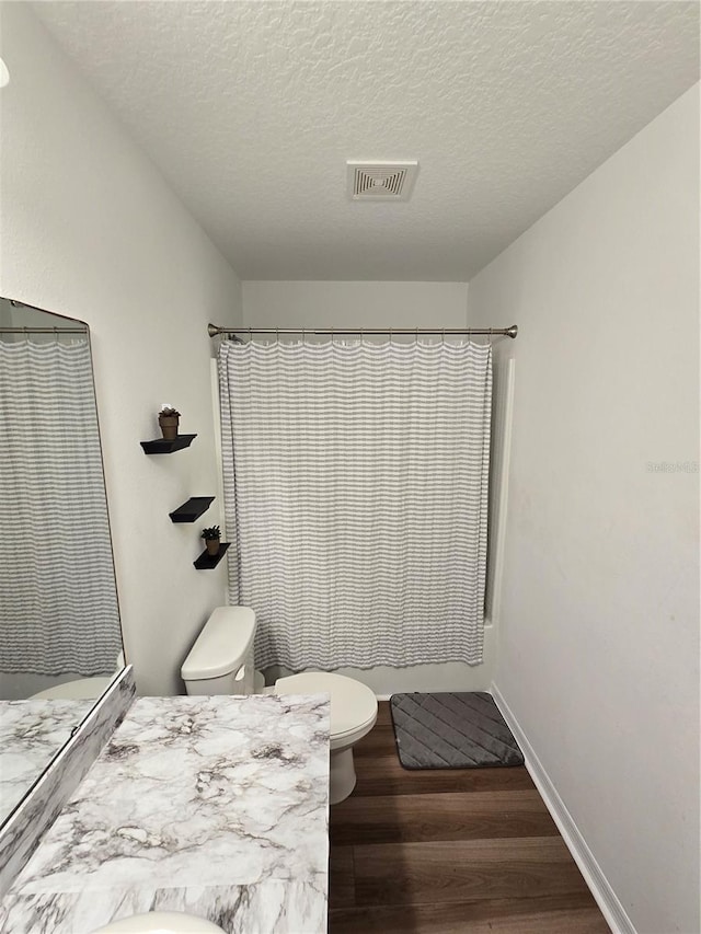 bathroom featuring hardwood / wood-style flooring, toilet, a textured ceiling, and a shower with shower curtain